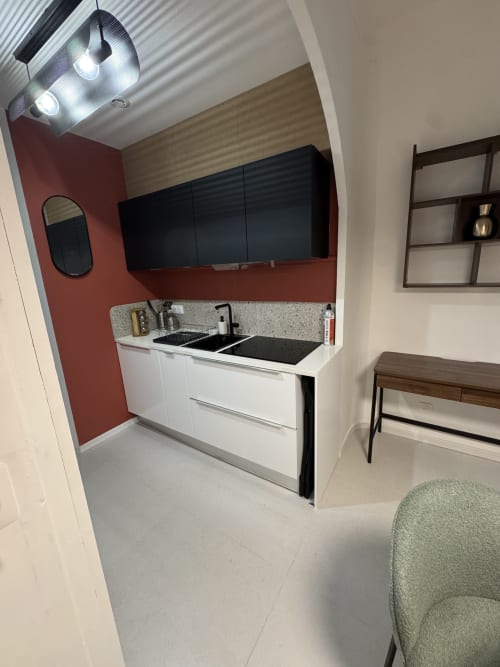 Modern kitchenette at Cosy Cottage By Alice in Bouc Bel Air with white cabinets, black stovetop, red accent wall, and