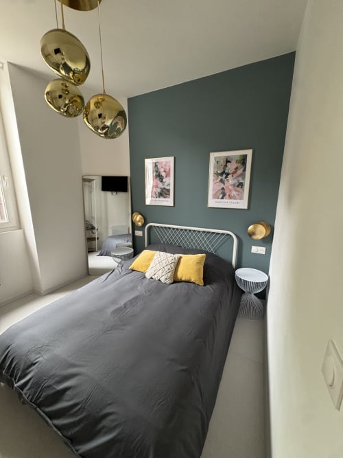 Modern bedroom at Cosy cottage By Alice in Bouc Bel Air with grey bed, yellow accents, teal accent wall, and brass pendant