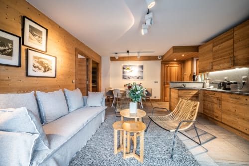 Modern alpine apartment living room with wooden walls, blue sofa, dining area, and kitchen at Le Chalet Mont-Blanc, Les