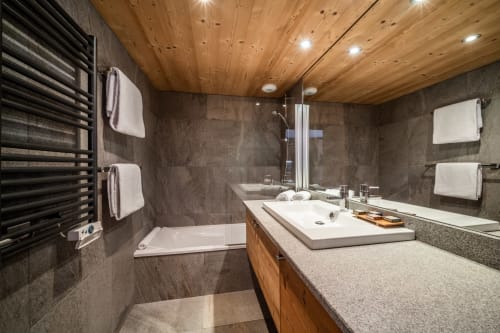 Modern bathroom in Le Tetralyre apartment at Le Chalet Mont-Blanc, Les Houches, with wooden ceiling, dark tile, and vanity
