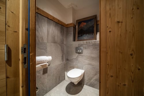 Modern bathroom with gray tiled walls, white toilet, and wooden accents at Le Chalet Mont-Blanc in Les Houches