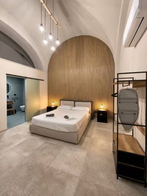 Suite moderna a Bari con parete in legno ad arco, letto bianco, luci sospese e arredi eleganti