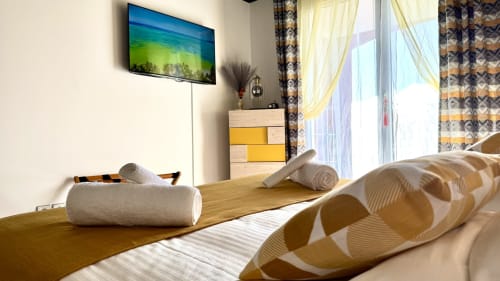 Helles Schlafzimmer in Studio-Wohnung in Cannes mit Flachbildschirm-TV, Holzmöbeln, aufgerollten Handtüchern und gemusterten Vorhängen