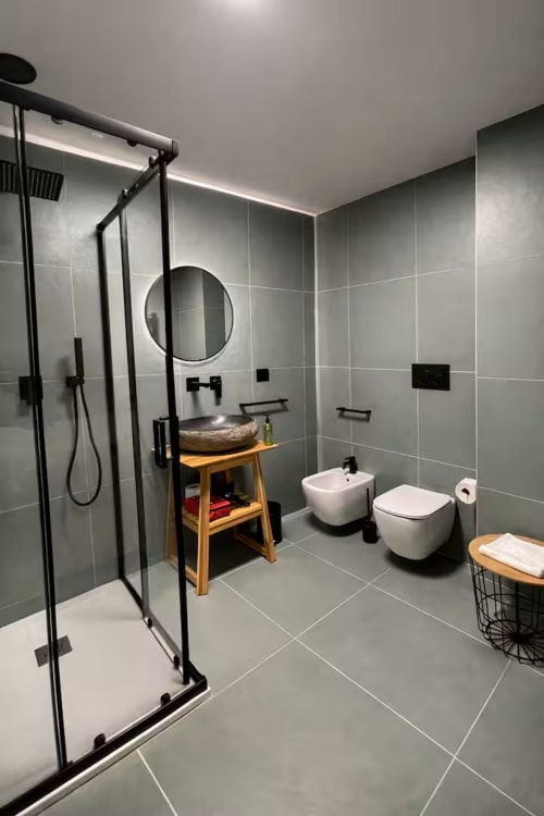 Moderno bagno nella suite 169 dell'appartamento La Grotta SPA di Bari. Bagno rivestito in piastrelle grigie con doccia, doppio wc e mobile lavabo in legno