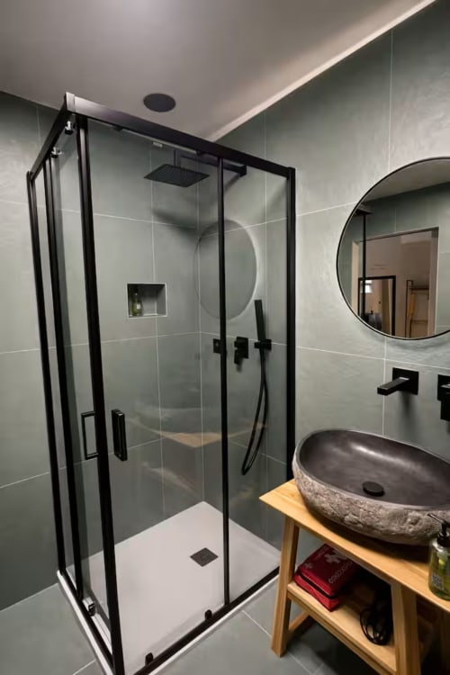 Bagno moderno nell'appartamento Suite169 La Grotta con box doccia in vetro e cornice nera, lavabo in pietra e specchio rotondo