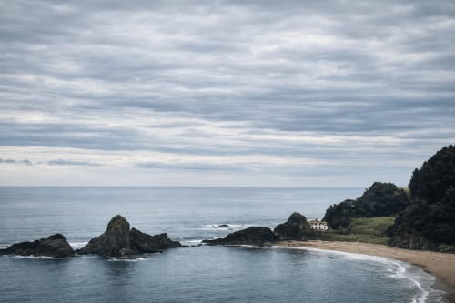 Vista del acantilado costero de la playa de Mutriku con afloramientos rocosos y una casa tradicional rodeada de vegetación verde