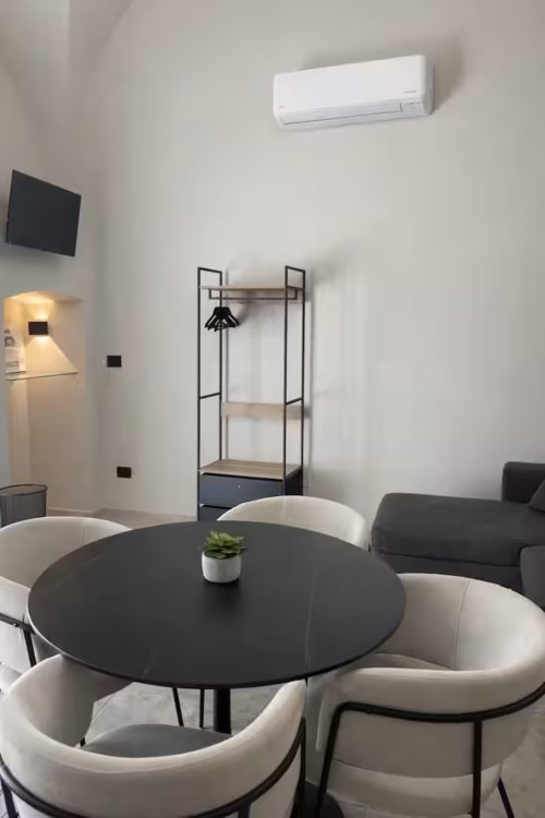 Elegante sala soggiorno della Suite169 a Bari con tavolo rotondo nero, sedie bianche, TV a parete e climatizzatore