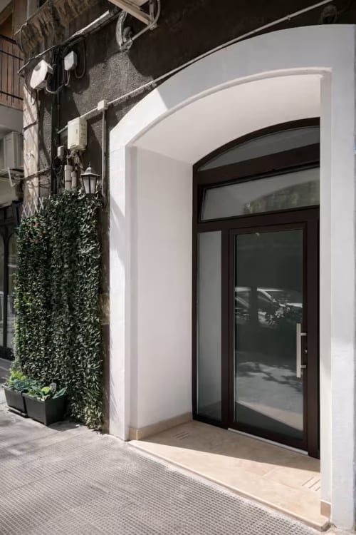 Ingresso moderno dell'appartamento Suite169 a Bari con porta in vetro scuro, cornice bianca curva e fioriera di edera