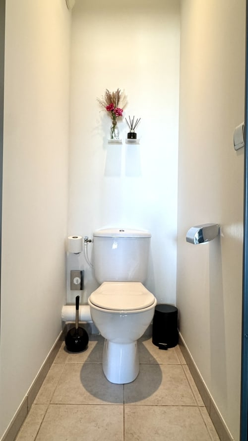 Modernes Badezimmer im Studio Château des Artistes mit weißem WC, beheiztem Handtuchhalter und dekorativen Blumen auf Wandregal