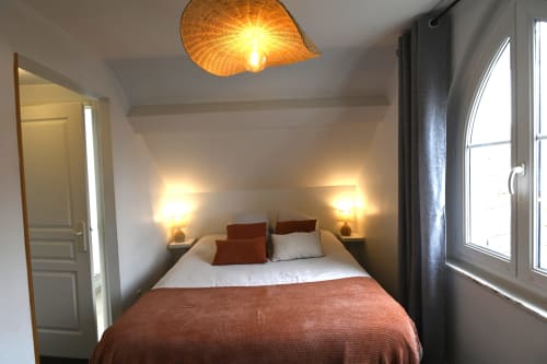 Chambre douillette au Gîte Le Ciel à Étretat avec lampadaire en fibres tressées, luminaires de chevet chaleureux et vue sur la ville