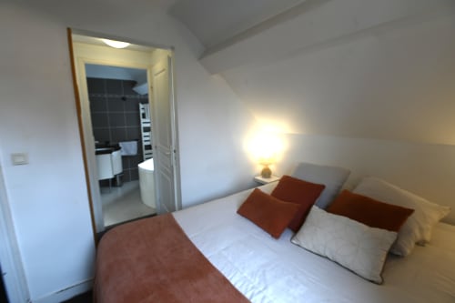 Chambre cosy du Gîte Le Ciel à Étretat avec lit double, oreillers marron, salle de bain attenante et lampe de chevet