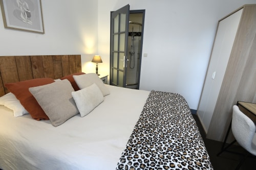 Chambre moderne au Gîte La Pierre à Étretat avec lit queen-size, tête de lit en bois, jeté léopard et salle d'eau attenante