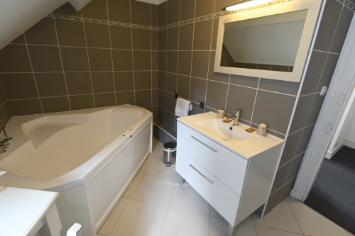 Salle de bain moderne du Gîte La Terre à Étretat avec vasque blanche, baignoire, miroir chauffant et carrelage noir