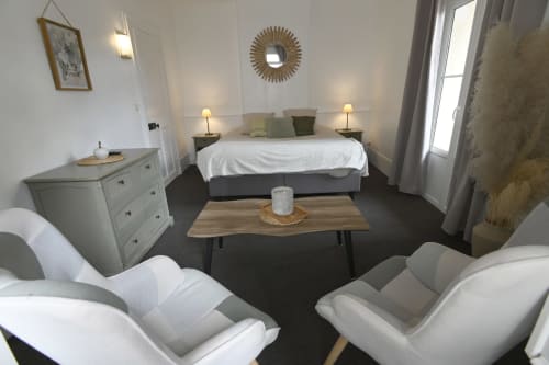 Chambre élégante au Gîte La Mer à Étretat avec lit queen-size, coin lounge moderne, commode et portes donnant sur la ville