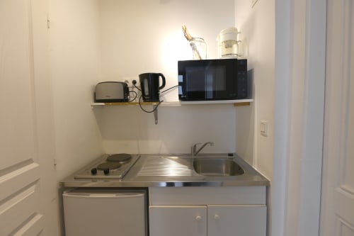 Kitchenette compacte du gîte La Mer à Étretat avec cuisinière, évier, micro-ondes et électroménagers sur étagère murale
