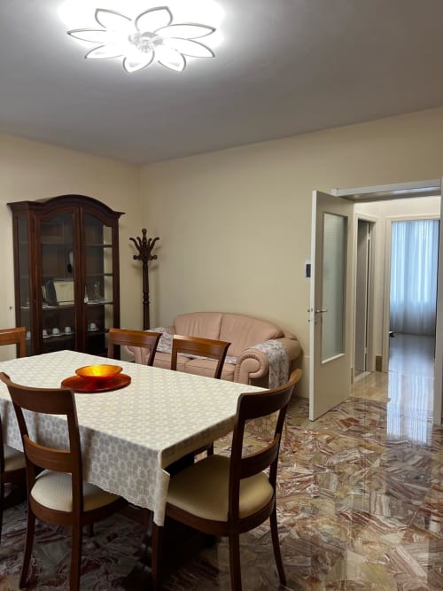 Sala da pranzo dell'appartamento di Atessa con tavolo in legno, sedie, pareti beige e lampada a soffitto a forma di fiore