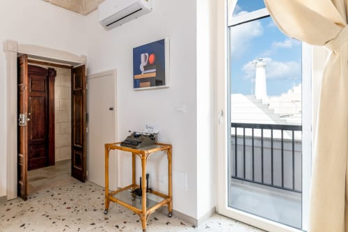 Ingresso della Suite Alimede a Trulli Life, Bari: porte in legno, scrivania con macchina da scrivere e balcone con vista sul faro