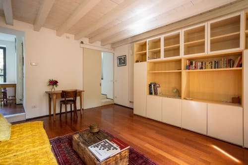 Sala de estar moderna con pisos de madera, estanterías empotradas, zona de trabajo y vistas al jardín en Bassano del Grappa, Italia