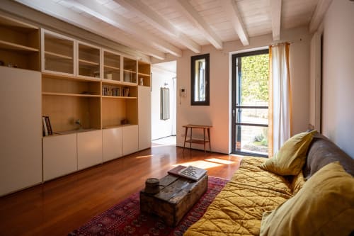 Luminosa sala de estar moderna con suelos de madera, sofá amarillo, almacenamiento integrado y vistas al jardín en Bassano del Grappa