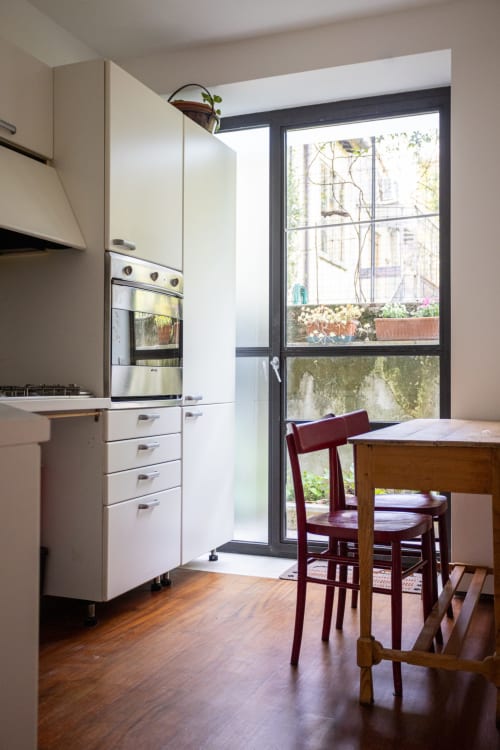 Cocina moderna con gabinetes blancos, horno de acero inoxidable, mesa de comedor de madera con sillas burgundy y vistas al jardín