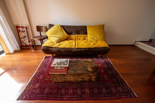 Luminosa sala de estar con sofá marrón, cojines amarillos, mesa de café de madera, alfombra roja estampada y pisos de madera en Borgo