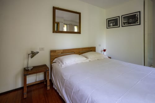 Dormitorio moderno con cama de madera, ropa de cama blanca, lámpara de escritorio, espejo y cuadros en el apartamento Borgo Margnan