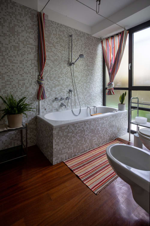 Baño moderno con paredes de mosaico, bañera con ducha, lavamanos redondo, piso de madera y ventana con vista al jardín en Kamalahouse