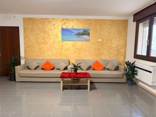 Modern triple room at TMS Hotel Mestre with beige sofa, orange cushions, and tropical beach artwork on gold accent wall