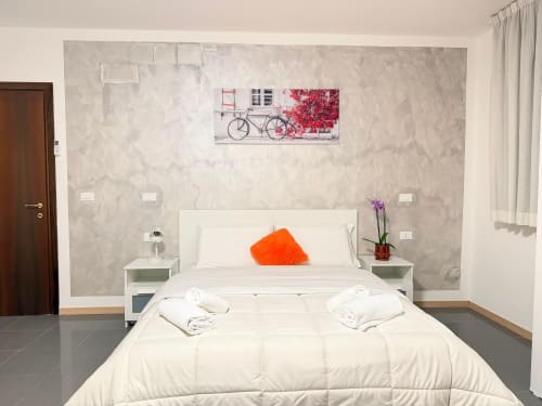 Camera moderna del TMS S.r.l. a Mestre con letto bianco, cuscino arancione e quadro con bicicletta