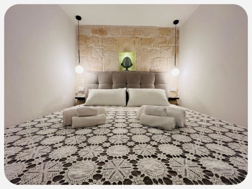 Camera da letto minimalista all'hotel Dimore Adua di Ostuni con testata beige, lampade a sospensione, muro in pietra e dettagli decorativi