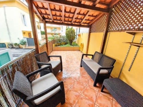 Terraço coberto com cadeiras de vime preto e almofadas brancas, azulejos em terracota, pérgola de madeira e paredes amarelas