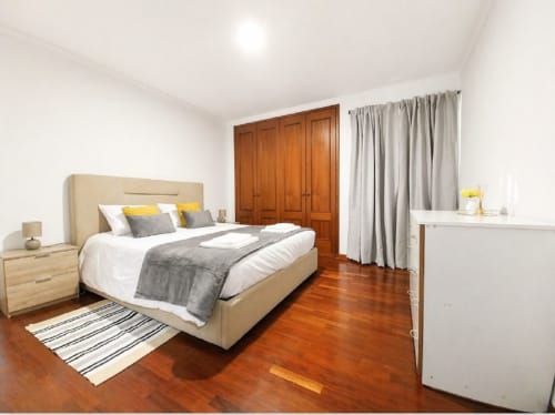 Quarto claro Brava Living em Funchal com cama bege, guarda-roupa de madeira, assoalho de madeira e vista para a cidade