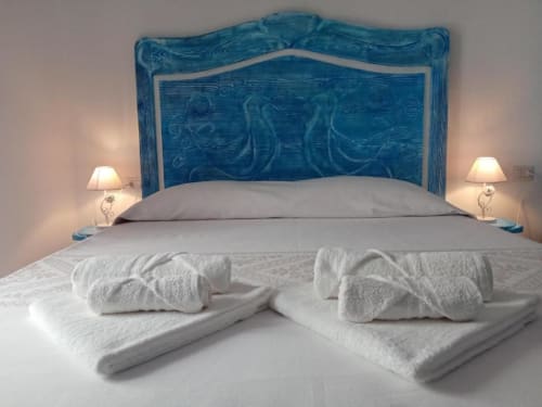 Lussuosa camera da letto a Regnos Altos Boutique Rooms a Bosa con testiera blu intagliata, biancheria bianca e asciugamani arrotolati