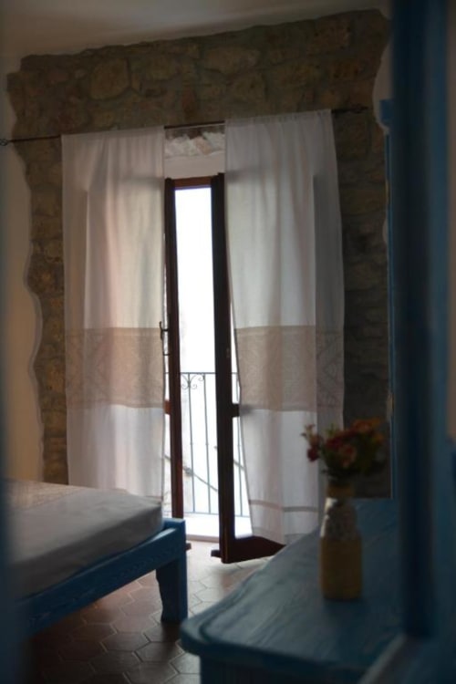Camera soleggiata con porta-finestra aperta e tende bianche presso Regnos Altos Boutique Rooms a Bosa, Italia