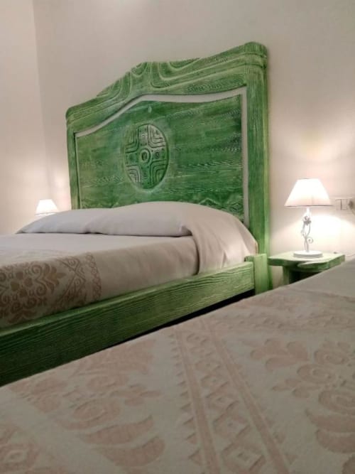 Testata del letto in legno intagliato verde presso Regnos Altos Boutique Rooms a Bosa, con biancheria bianca e lampada da comodino