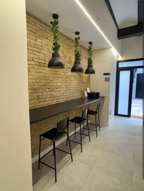Área de trabajo moderna en Be Gonfre Flats Valencia con pared de ladrillo visto, mesada oscura, taburetes negros y tres lámparas colgantes