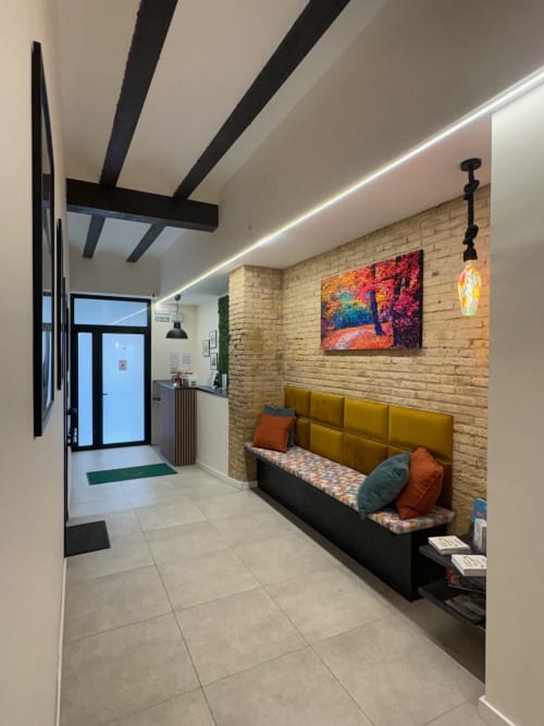 Habitación doble moderna en Be Gonfre Flats Valencia con sofá mostaza, ladrillo visto, vigas negras y obras de arte coloridas