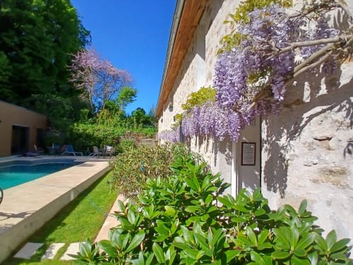 Clos De La Gourmandiere courtyard with wisteria-draped stone walls, pool, and manicured gardens in Saint-Lothain