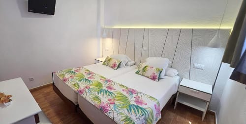 Quarto moderno nos Apartamentos Gelimar Porto Rico com camas gêmeas, passadeira floral e iluminação ambiental no teto