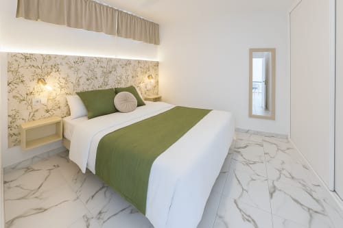Quarto moderno em Apartamentos Gelimar Puerto Rico com cama queen, acentos verdes, cabeceira floral e piso de mármore