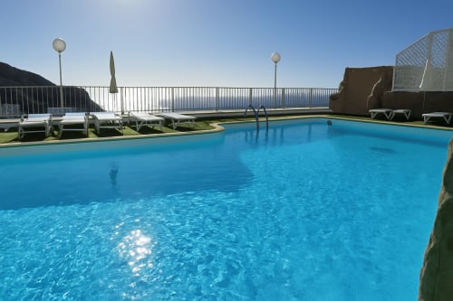 Piscina azul brilhante com espreguiçadeiras e guarda-sóis no Apartamentos Gelimar em Porto Rico, com vista para o mar