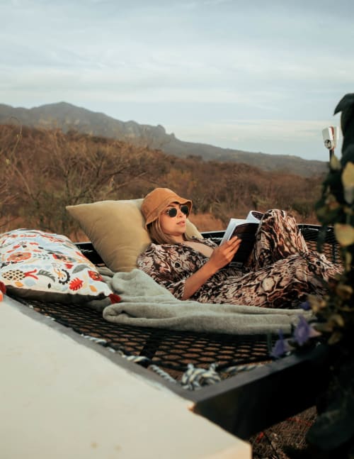 Mujer leyendo en cama al aire libre en Meraki Glampings con vistas a las montañas, Malinalco