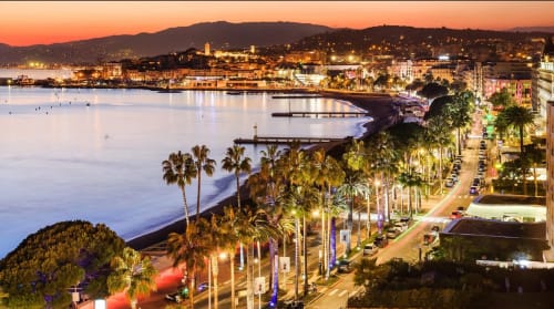 Tramonto mediterraneo sulla costa con lungomare affacciato sulla spiaggia, palme e edifici illuminati sul waterfront