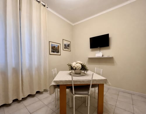 Dining area in Verona apartment with table, white chairs, TV, framed artwork and cream curtains