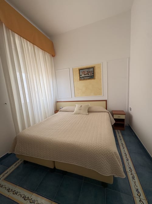 Camera accogliente a Casa Mannini B&B a Maiori con copriletto color crema, testata in legno e finestra con vista sulla città