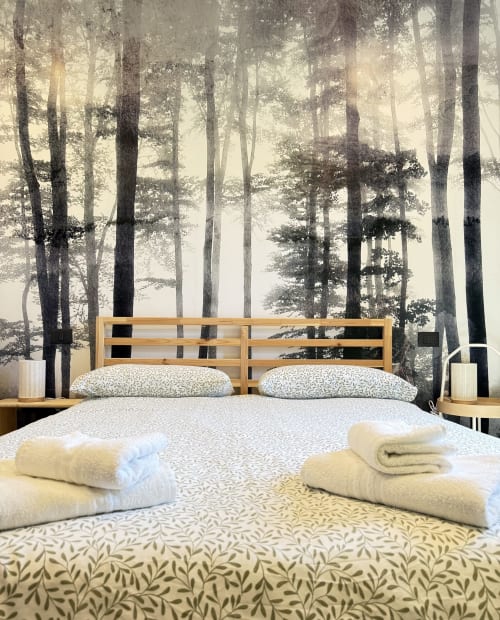 Camera matrimoniale accogliente al B&B Luna Verde con letto in legno, asciugamani bianchi e sfondo con carta da parati foresta nebbiosa