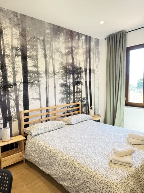 Camera da letto del B&B Luna Verde con letto in legno, carta da parati con bosco, tende verdi e vista sulle montagne dalla finestra