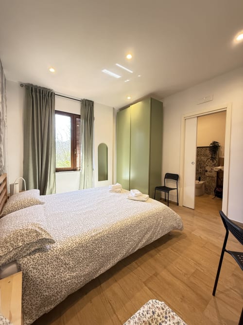 Camera moderna della B&B Luna Verde con letto matrimoniale, guardaroba verde, finestra con vista sul giardino, pavimento in legno e bagno en suite