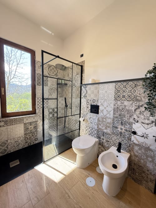 Bagno moderno della B&B Luna Verde con piastrelle decorate, box doccia con cornice nera, WC, bidet e vista montagna