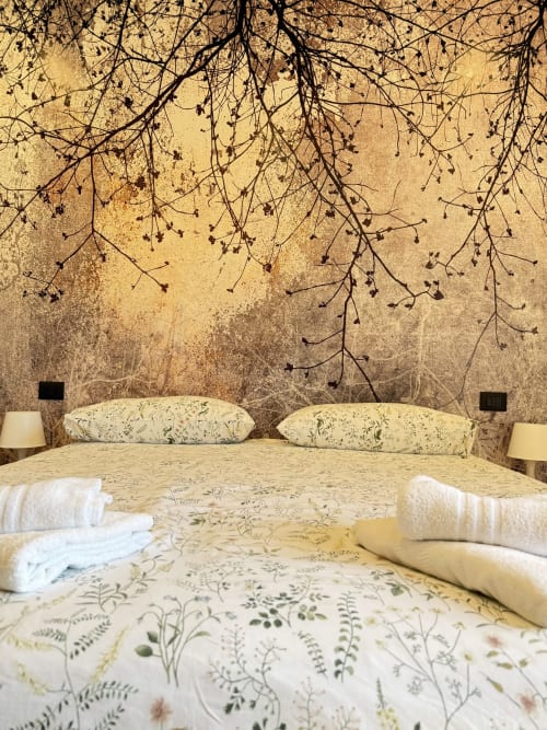 Camera accogliente al B&B Luna Verde con murale botanico, biancheria color crema con motivi floreali e eleganti rami sospesi